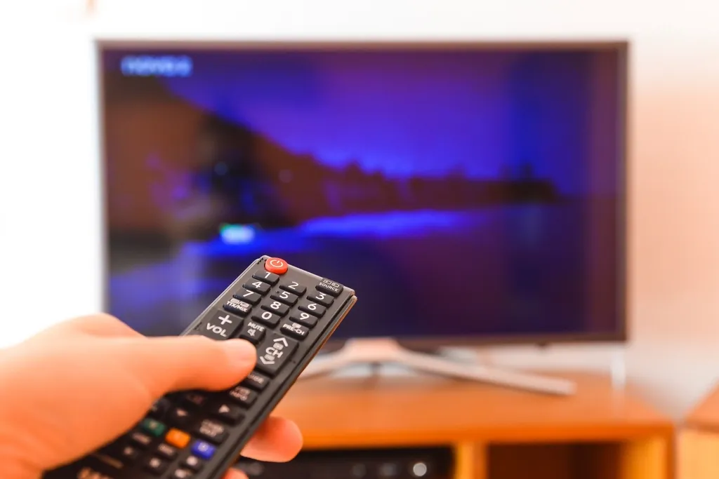 Hand pointing a remote control at a flat-screen TV, illustrating the ZYMINEX guide to choosing a plan and number of devices
